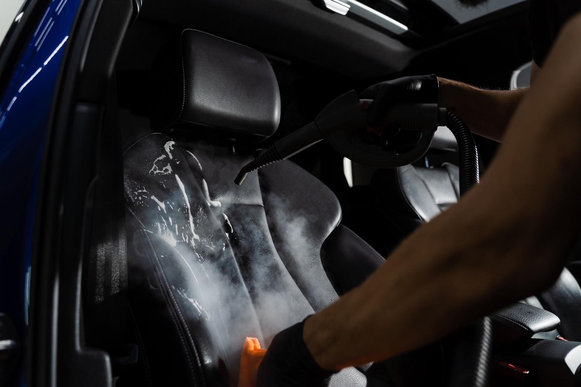 Steam cleaning of leather seat after foam and detergent washing. Worker in auto cleaning service clean car inside. Car interior detailing.